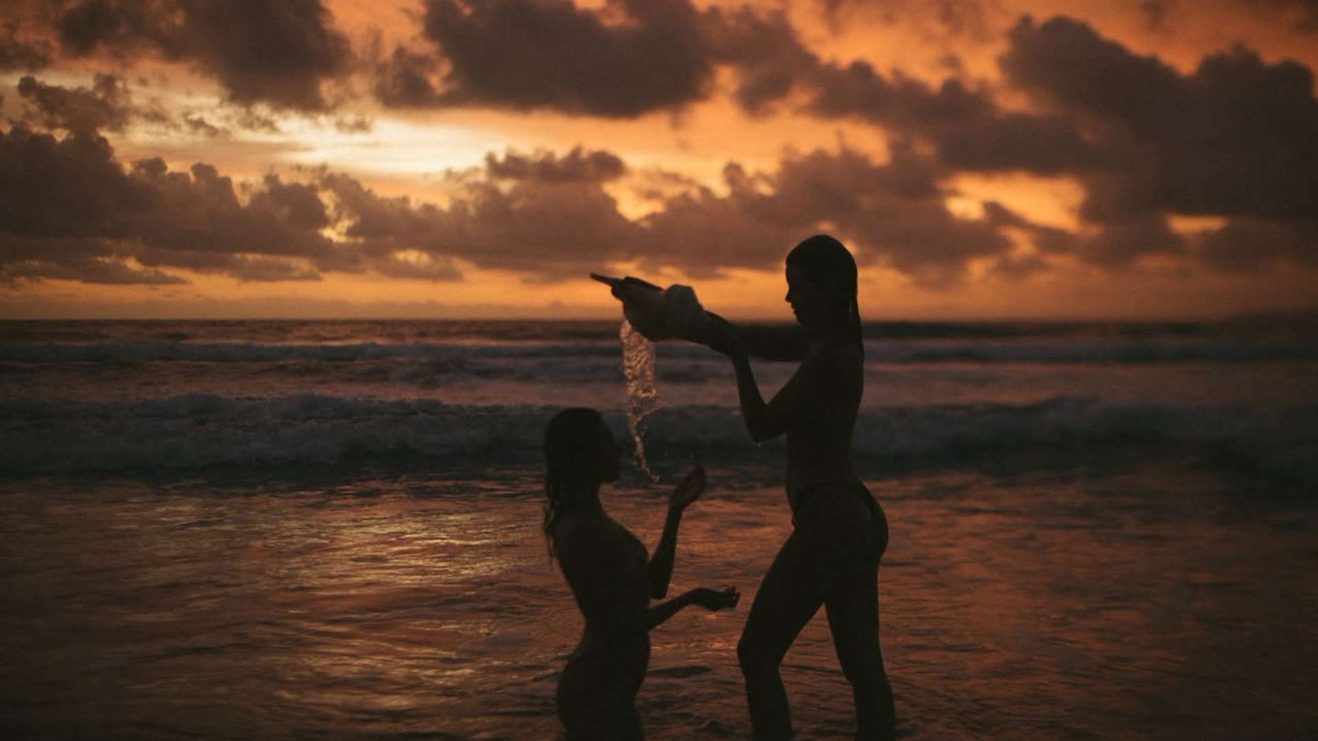 Women holding a water ceremony at sunset by the ocean