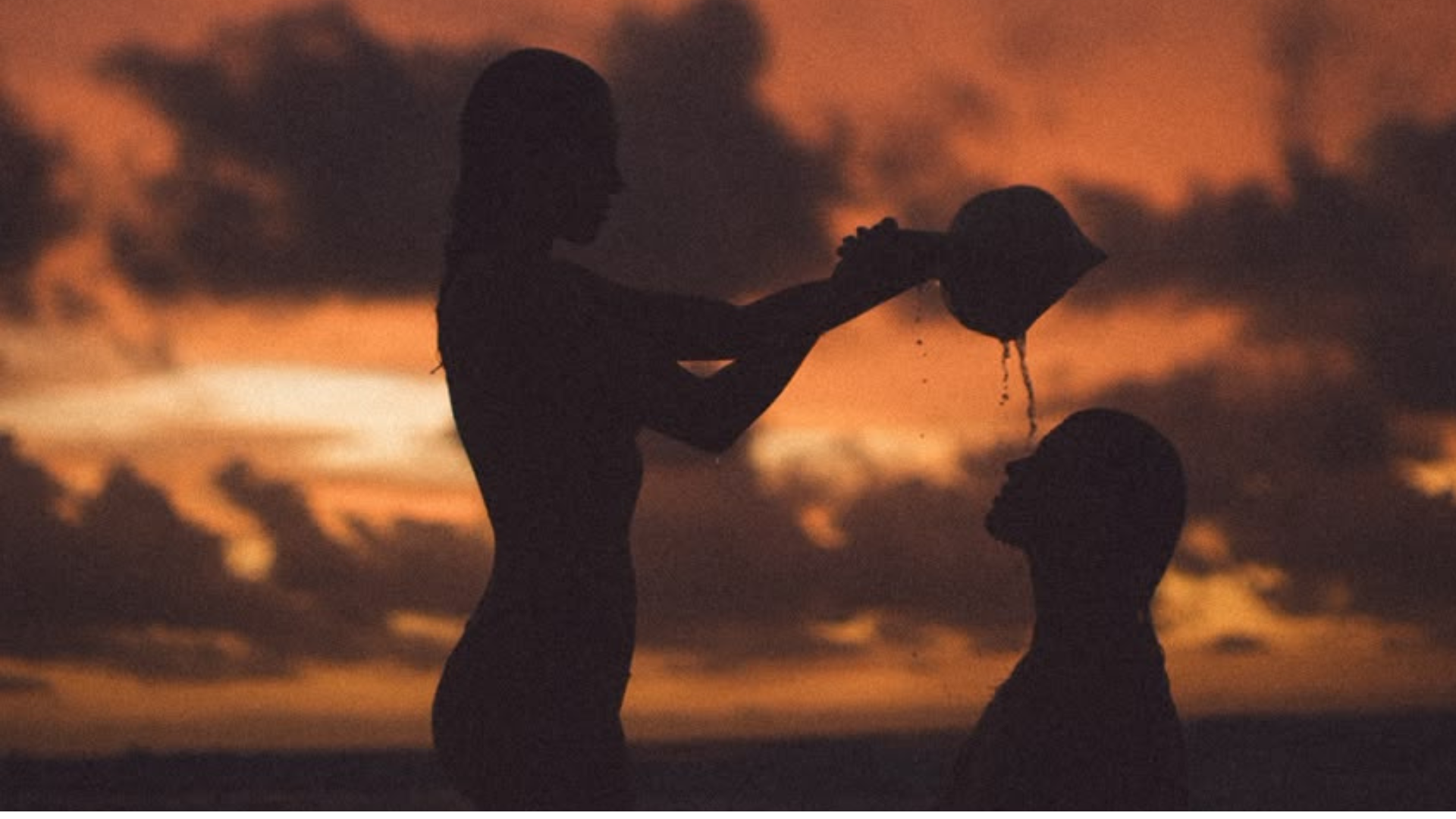 Two women in silhouette at sunset, water poured in ritual
