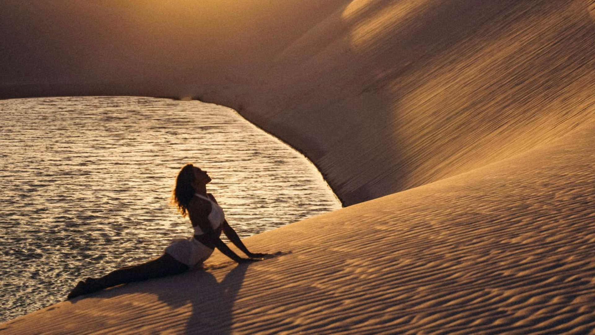 Woman in a yoga pose on golden dunes at sunrise