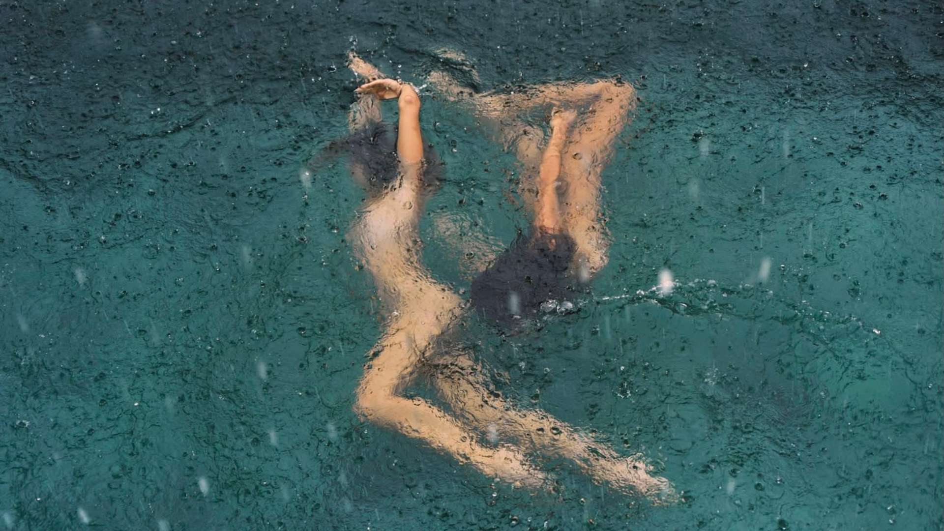 Woman floating in turquoise water under soft rain